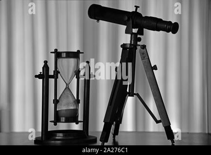 Silhouettes of a Hourglass and a telescope on a bookcase shelf. Concept : technology, exploration, science, observation, time etc. Stock Photo