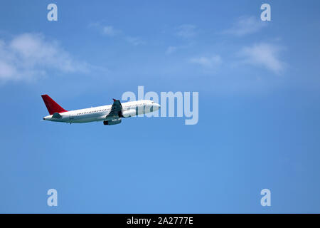 Airplane flying in the blue sky on background of white clouds, side view. Two-engine commercial plane during the turn, turbulence and travel concept Stock Photo