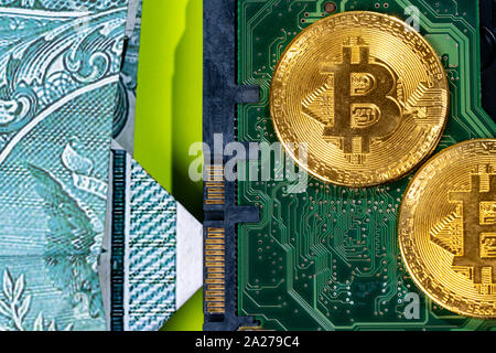 Concept of Bitcoin Mining. A little miner is digging for bitcoin with graphic card dollars. Golden Bitcoin on the green microchip board with dollars. Stock Photo