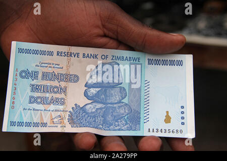 African man's hand holding a one hundred-trillion dollar note, Zimbabwe.