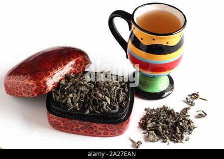 Loose green tea leaves in red box with colourful mug on white background Stock Photo