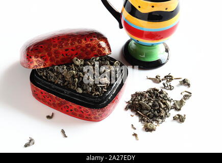 Loose green tea leaves in red box with colourful mug on white background Stock Photo