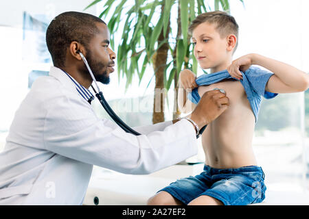 African male doctor and child boy patient. Smiling pediatrician man sees boy in medical office. African American male pediatrician with stethoscope Stock Photo