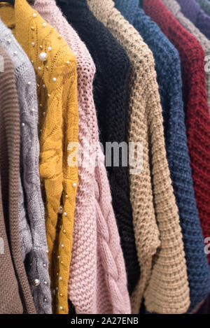 knitted sweaters and cardigans hang on a floor hanger. Colored big knitwear in the wardrobe Stock Photo