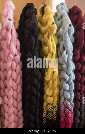 knitted sweaters and cardigans hang on a floor hanger. Colored big knitwear in the wardrobe Stock Photo