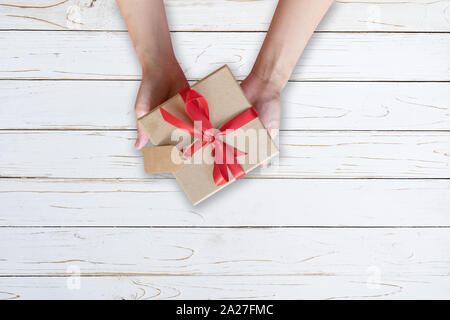 Woman hand holding gift box on wood plank and painted in white color with copy space. Stock Photo