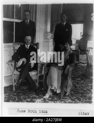 Pres. and Mrs. Calvin Coolidge, seated, full-length, in wicker arm chairs, with two sons standing behind them Stock Photo