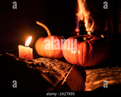 Two halloween pumpkins standing in the dark on birch logs surrounded by burning candles. In the background is a flame from a fireplace. Mystical holid Stock Photo