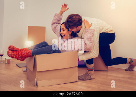 Handsome young man helping his laughing girlfriend riding a carton box Stock Photo