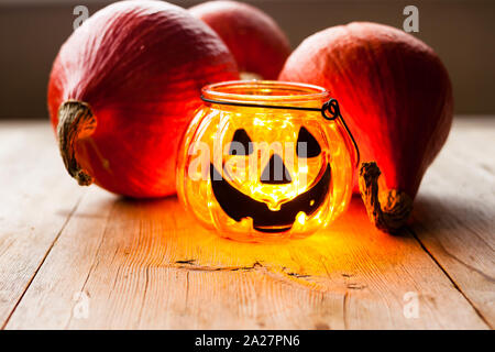 Halloween decoration concept. Scary jack-o-lantern candle holder with pumpkins on old wooden background. Selective soft focus. Shallow depth of field. Stock Photo