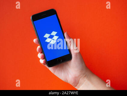 Kyiv, Ukraine - October 1, 2019: Studio shot of hand holding Apple iPhone 8 with Dropbox logotype on a screen. Isolated on an orange background. Stock Photo