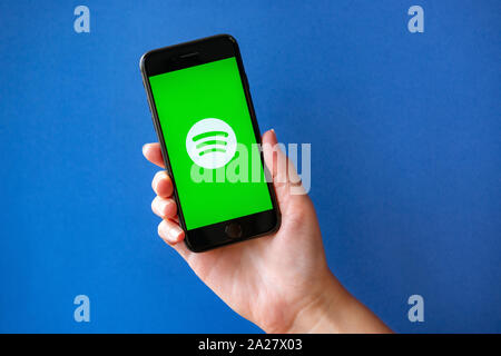 Kyiv, Ukraine - October 1, 2019: Studio shot of hand holding Apple iPhone 8 with Spotify logotype on a screen. Isolated on a blue paper background. Stock Photo