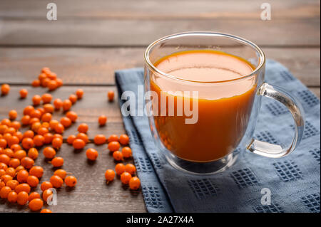 Healthy sea buckthorn juice in a transparent mug on a linen napkin on a wooden table. Berries are near. Rustic style. Stock Photo