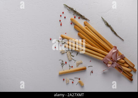 Traditional Italian breadsticks grissini lie on a light textured table. Near sprigs of rosemary Stock Photo