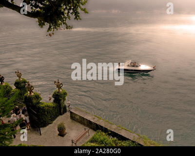 Lake Como, Lombardy, Italy. Tourists wait for their  ferry transport whilst a powerboat sppeds by Villa del Balbianello,  near Lenno, LAKE COMO