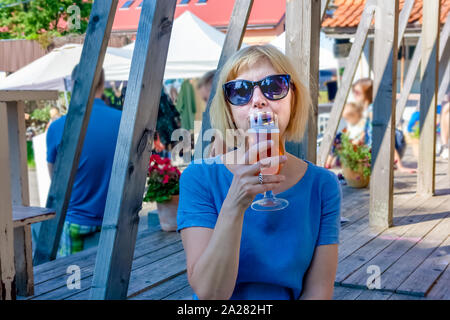 Woman drinking beer on sidewalk in cafe. A beautiful female model enjoys city life on a city square. Stock Photo