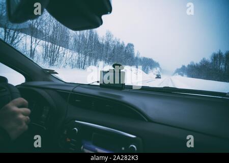 roadtrip - mans hands on the wheel and on a winter snowy road Stock Photo