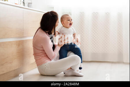 Adorable baby playing with mom, sitting on floor in kitchen Stock Photo