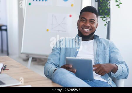 Cheerful business coach holding digital tab, sitting in modern office Stock Photo