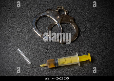 Handcuffs and a syringe with a dose of the drug on a black background Stock Photo