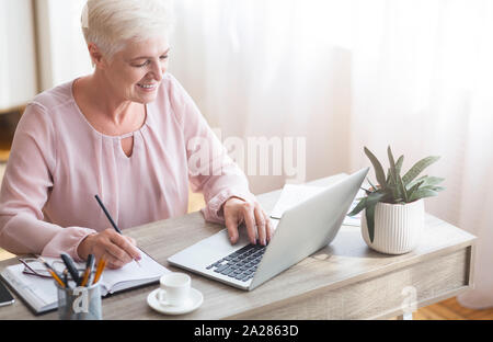Top view of mature working lady making notes, using laptop Stock Photo