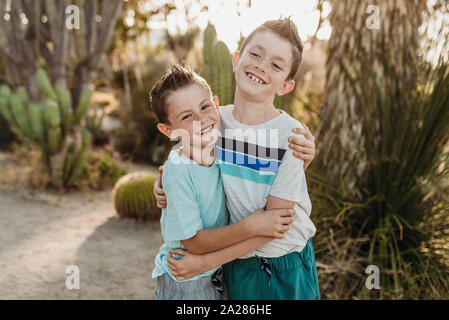 Cheerful brothers embracing and smiling in sunny cactus garden Stock Photo