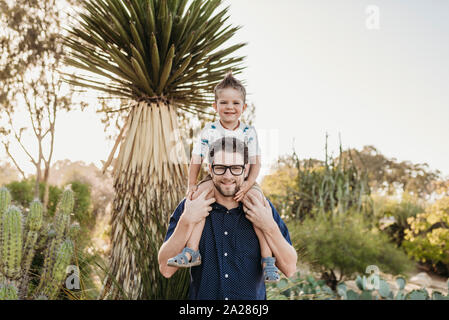 Young toddler boy sitting on father's shoulders in sunny cactus garden Stock Photo