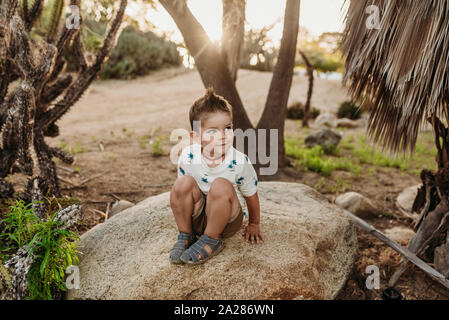 Portrait of young boy sitting on rock and smiling in cactus garden Stock Photo