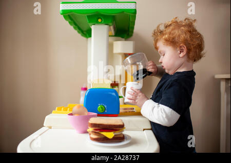 Toddler boy playing in toy kitchen pretending to pour coffee into cup Stock Photo