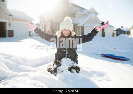 Girl 10-12 years old having fun in the snow in front of house Stock Photo