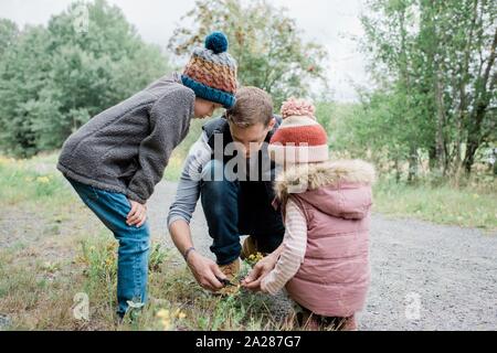 father showing his children how to cut flowers outside whilst walking Stock Photo