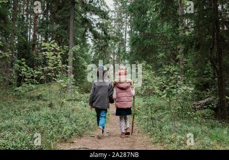 brother and sister holding hands walking through the woods in fall Stock Photo