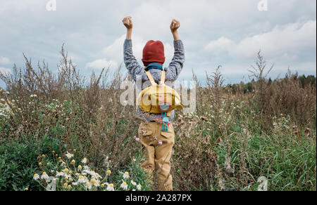 young school boy reaching up to the sky stood in a field of flowers Stock Photo