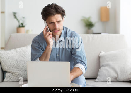 Guy Having Unpleasant Phone Conversation Working On Laptop At Home Stock Photo