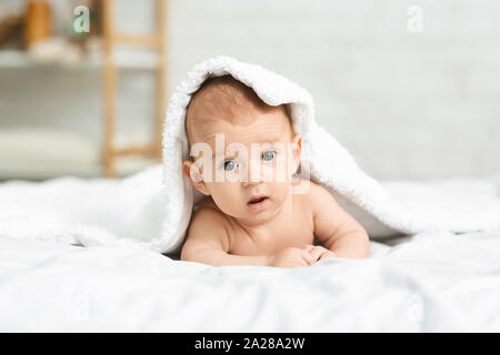 Portrait of cute newborn boy peeking out from under blanket Stock Photo