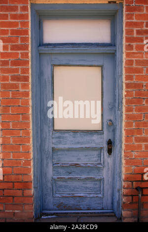 Distressed grey painted door set back in a red brick building doorway Stock Photo