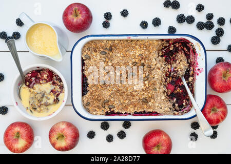 Homemade Blackberry and apple crumble and custard with a tablespoon. Organic Oat and seed crumble with foraged blackberries and apples Stock Photo