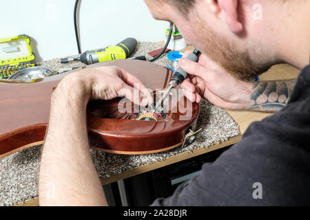 A Guitar Technician or tech, in his workshop, soldering a repair within the body of an electric guitar. Stock Photo