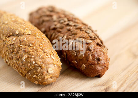 Long whole wheat sunflower seed bread roll and long whole wheat sesame seed bread roll on light wood. Stock Photo