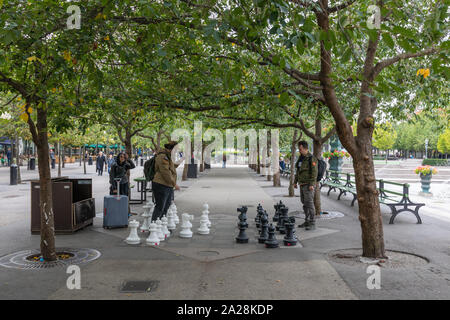 Stockholm, Sweden, September 2019: Two young men play chess outdoors with large chess pieces beneath an avenue of trees in Kungsträdgården. Stock Photo