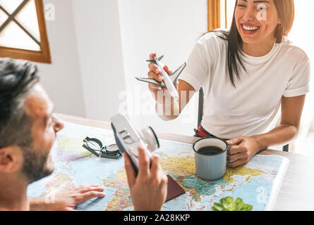 Happy couple having fun planning next world tour together - Young people getting ready for next trip using a travel map Stock Photo