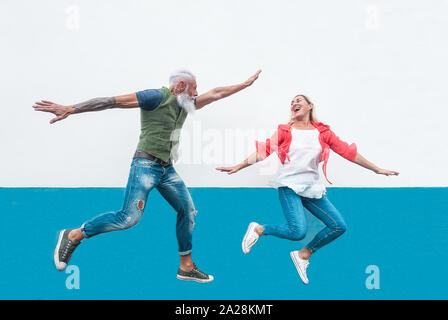 Happy seniors crazy couple jumping together outdoor - Mature trendy people having fun celebrating and dancing outside Stock Photo