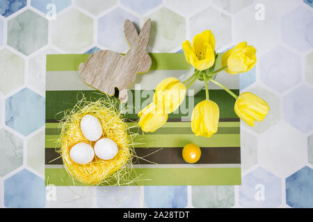 Colorful Easter decorations on a table, chicken eggs in a nest, yellow tulips in a white vase. Stock Photo