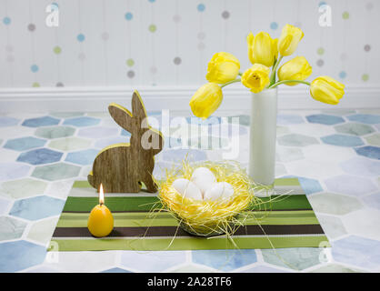 Easter decorations on a table, chicken eggs in a nest, yellow tulips in a white vase. Stock Photo