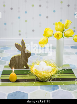 Easter decorations on a table, chicken eggs in a nest, yellow tulips in a white vase. Stock Photo
