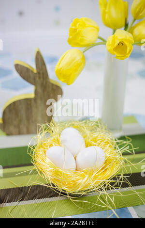 Easter decorations on a table, chicken eggs in a nest, yellow tulips in a white vase. Stock Photo