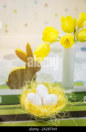 Easter decorations on a table, chicken eggs in a nest, yellow tulips in a white vase. Stock Photo