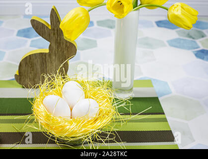 Easter decorations on a table, chicken eggs in a nest, yellow tulips in a white vase. Stock Photo