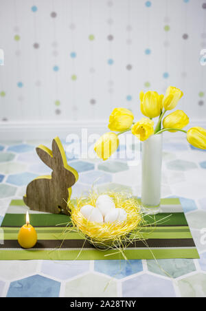 Easter decorations on a table, chicken eggs in a nest, yellow tulips in a white vase. Stock Photo