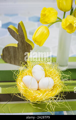 Easter decorations on a table, chicken eggs in a nest, yellow tulips in a white vase. Stock Photo